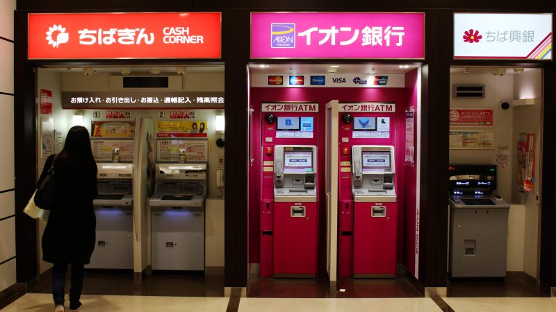 A customer approaches a row of ATMs (including Chiba Ginko and Aeon Ginko) in an Aeon Mall in Makuhari. Japanese regional banks are under pressure due to demographic shifts and the COVID-19 pandemic.