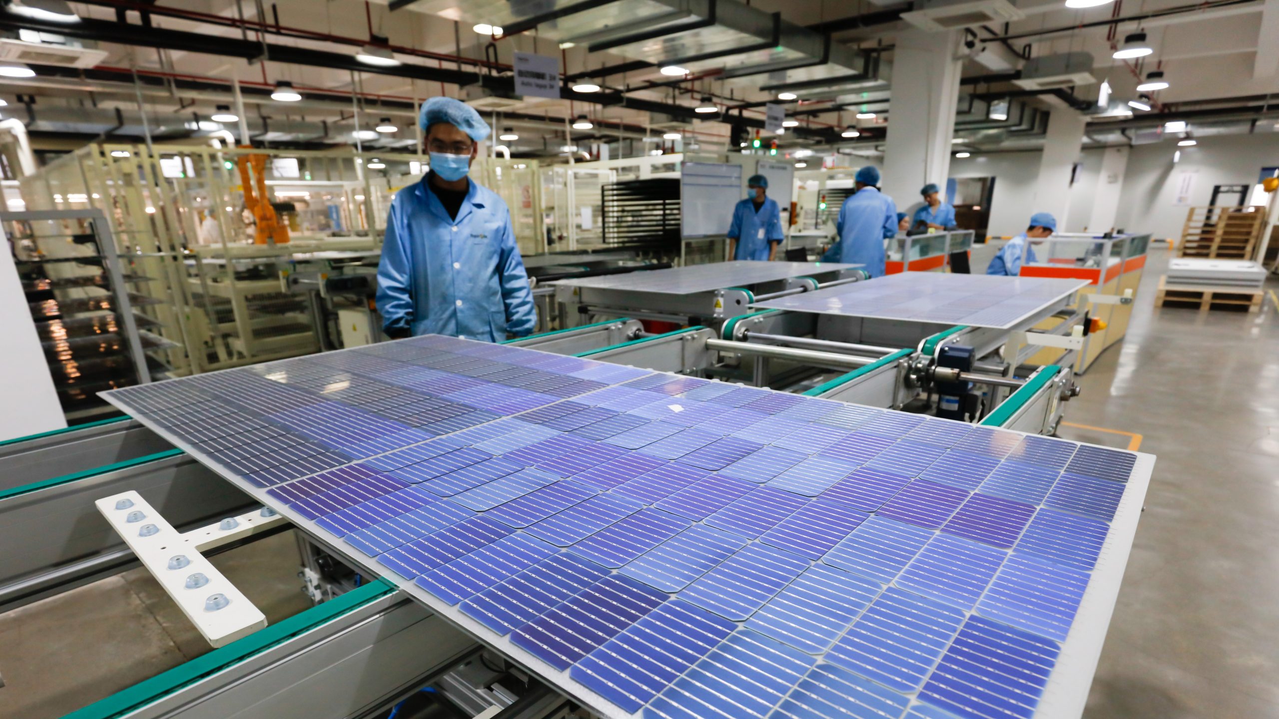 Workers operate equipment to produce photovoltaic circuit boards at a production workshop of a green energy technology company